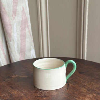 White mug with green rim on a dark wooden table against a neutral wall.