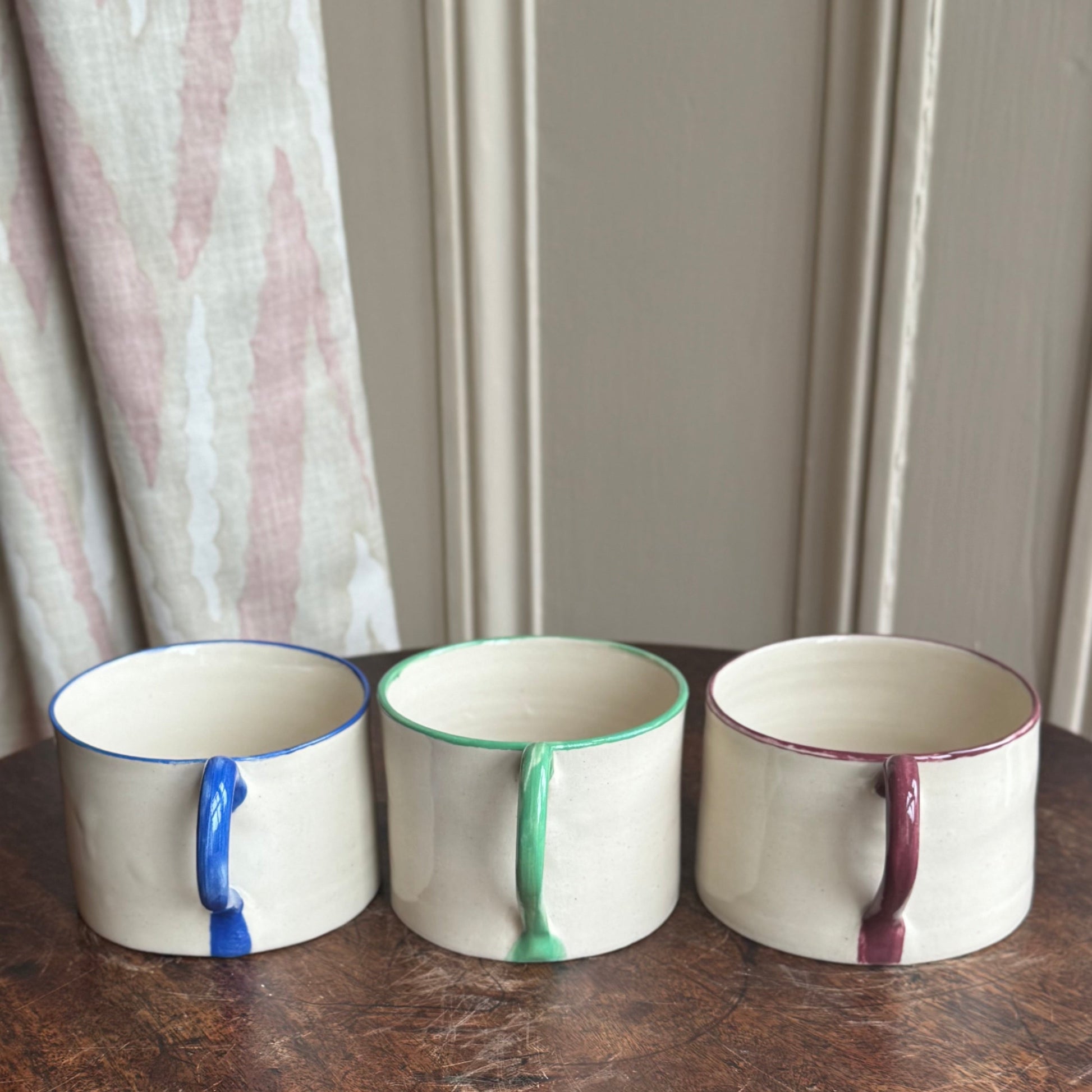 Three ceramic mugs with unique color patterns on a wooden table.