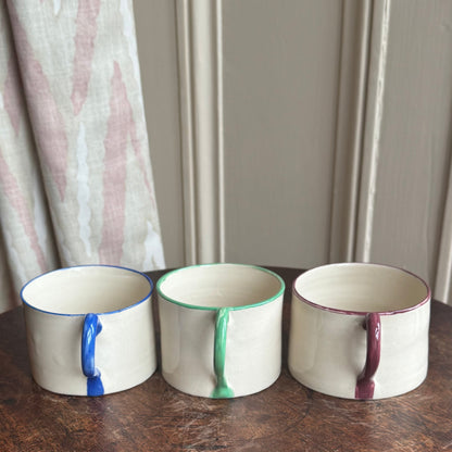 Three ceramic mugs with unique color patterns on a wooden table.