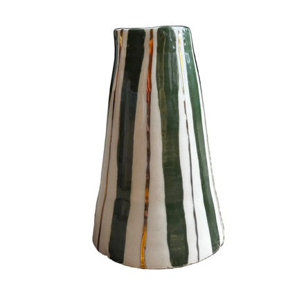 A small tapered ceramic vase with vertical green, white, and thin gold stripes, standing on a textured beige carpet in an indoor room setting.