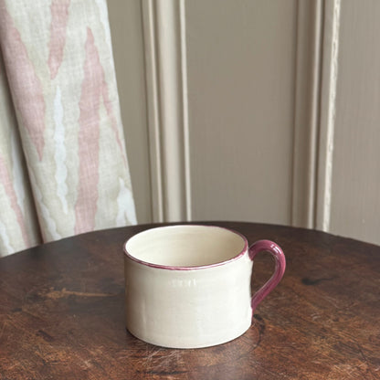 Stoneware hand thrown mug on a dark wooden table with a neutral background and burgundy rim and handle