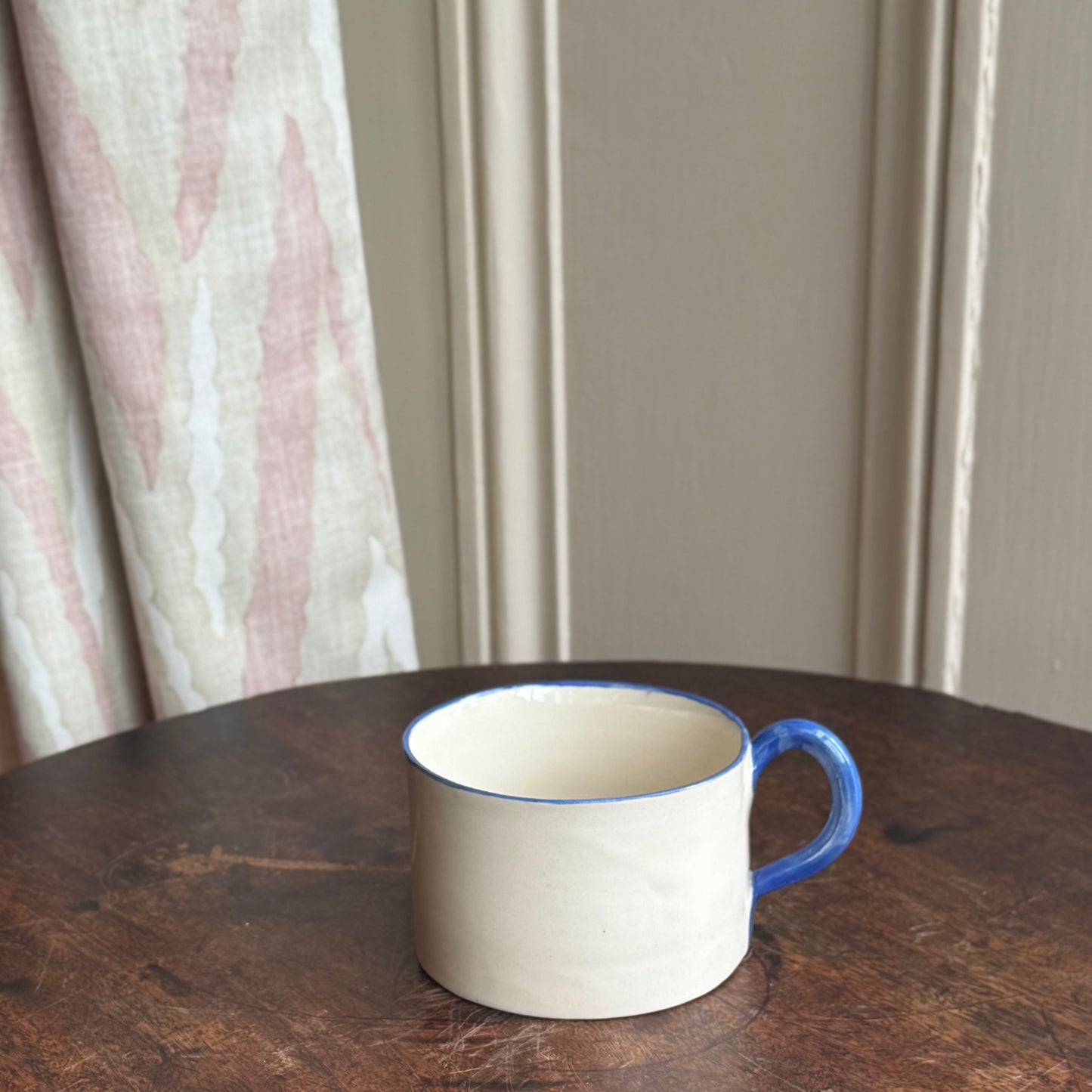 White mug with blue handle on a wooden table against a neutral wall.