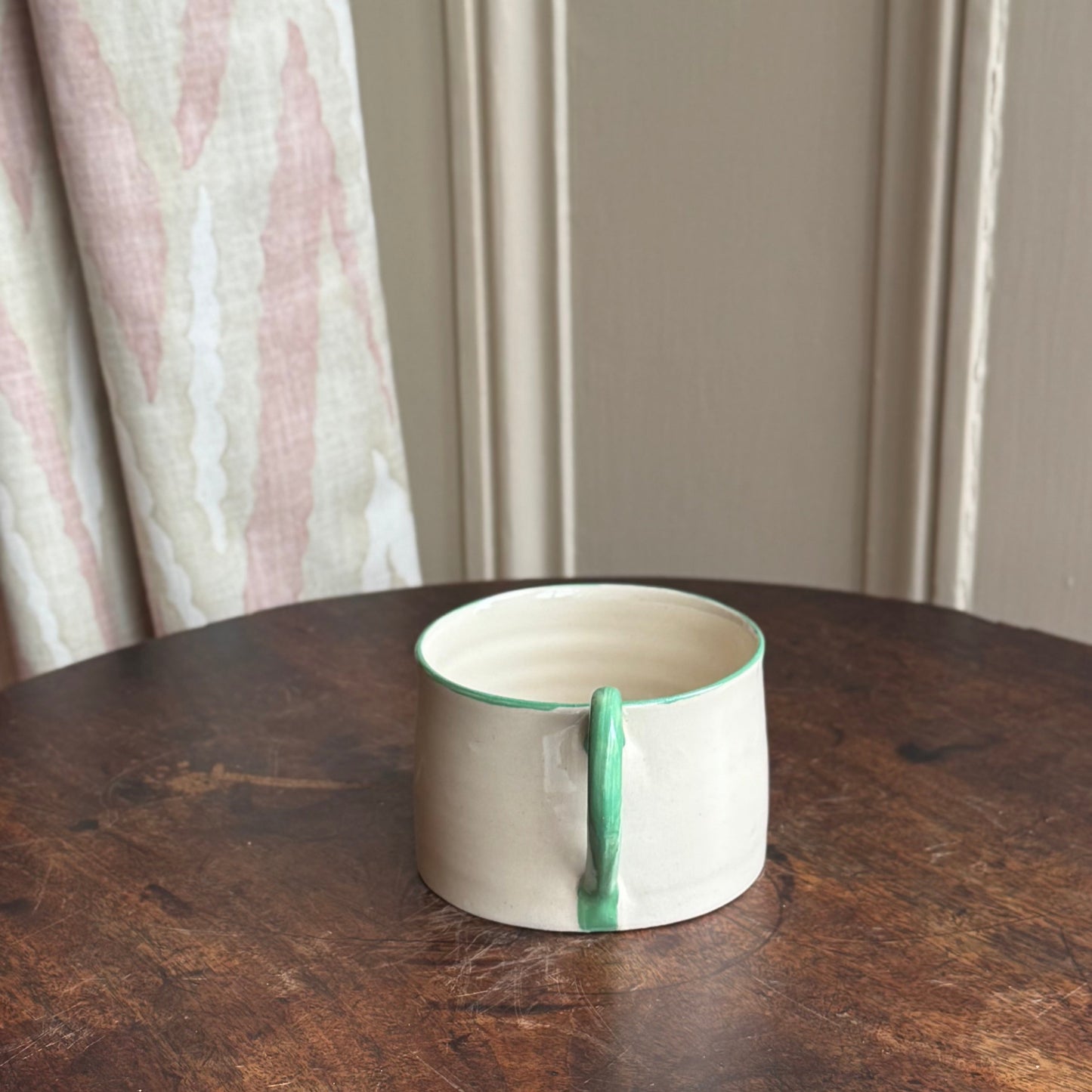 Ceramic mug with green interior on a wooden table against a neutral wall.