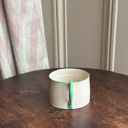 Ceramic mug with green interior on a wooden table against a neutral wall.