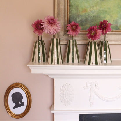 Five striped glass vases filled with pink flowers arranged on a white fireplace mantel against a peach-pink wall, with framed wall art in the background.