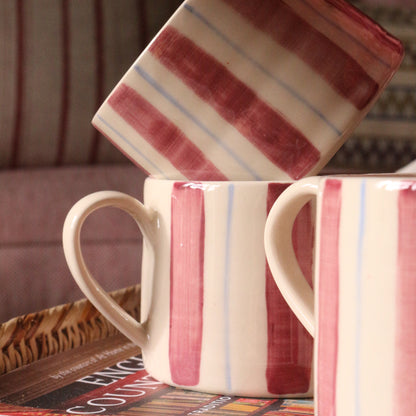 Three ceramic mugs with a cream base and burgundy and light blue stripes, styled on a tray with a book in a cozy indoor setting.